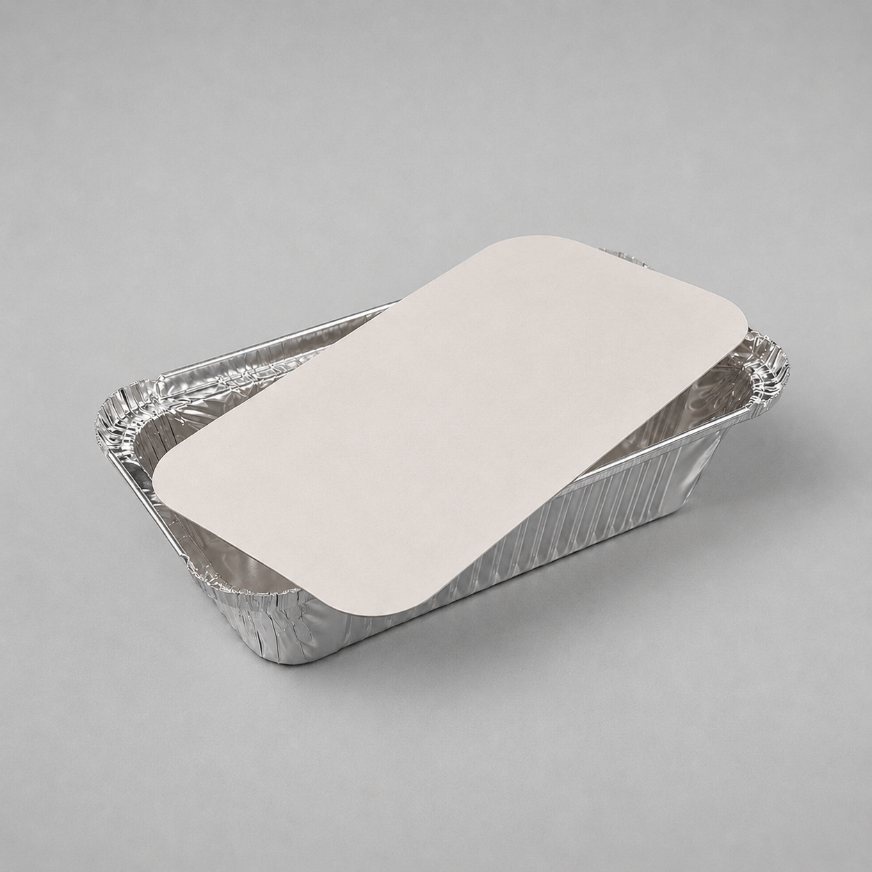 6A rectangular aluminum foil tray with a flat, light beige paper liner placed on top, photographed on a neutral gray background.