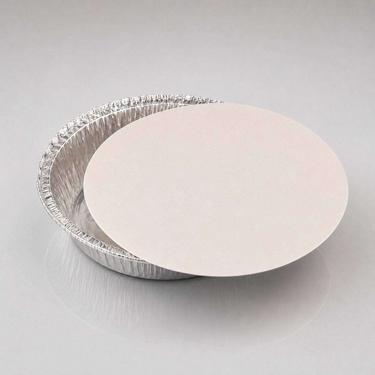 A 9 inch round silver aluminum pie tin with a smooth, light beige circular insert or lid resting on top, photographed on a neutral light gray background.