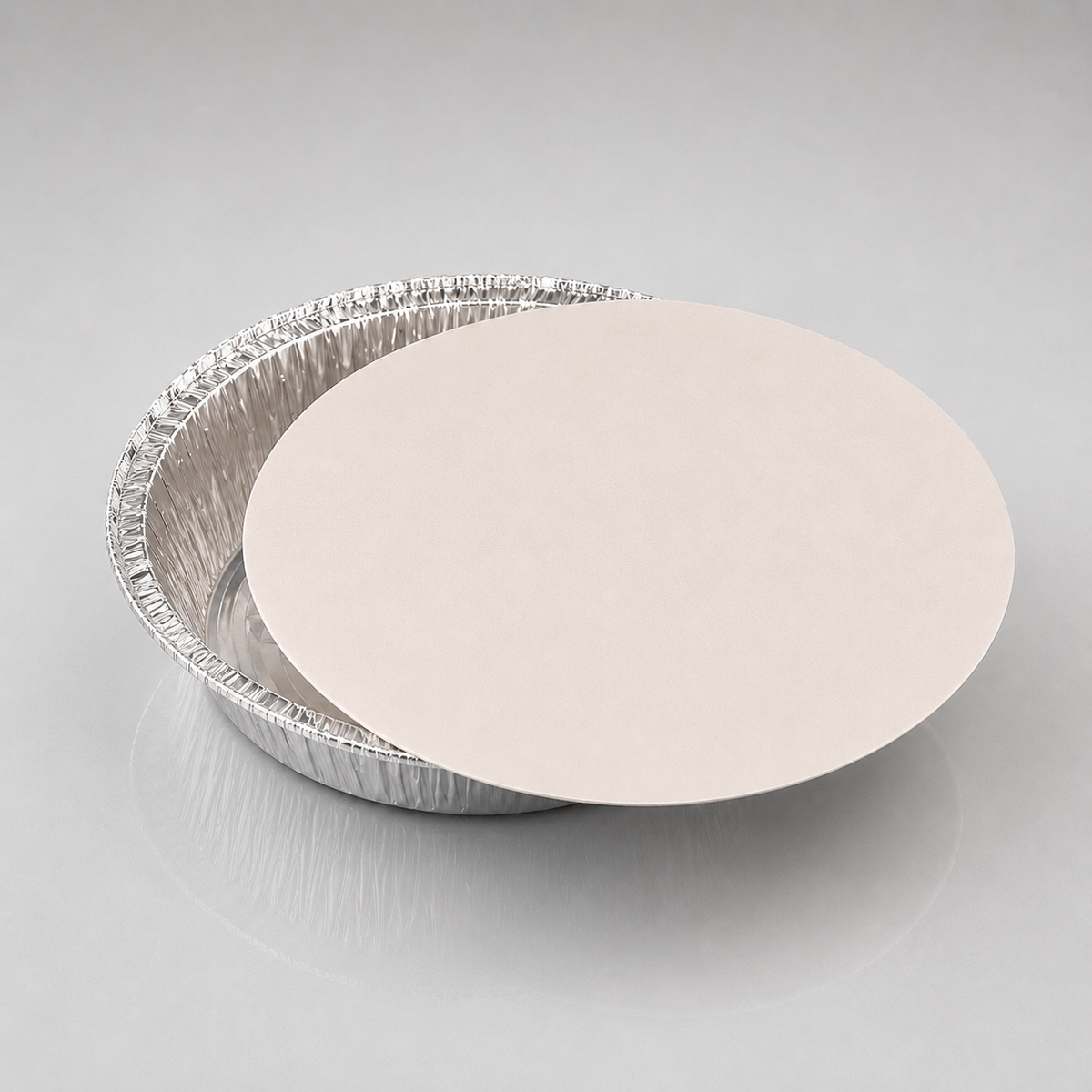 A 9 inch round silver aluminum pie tin with a smooth, light beige circular insert or lid resting on top, photographed on a neutral light gray background.