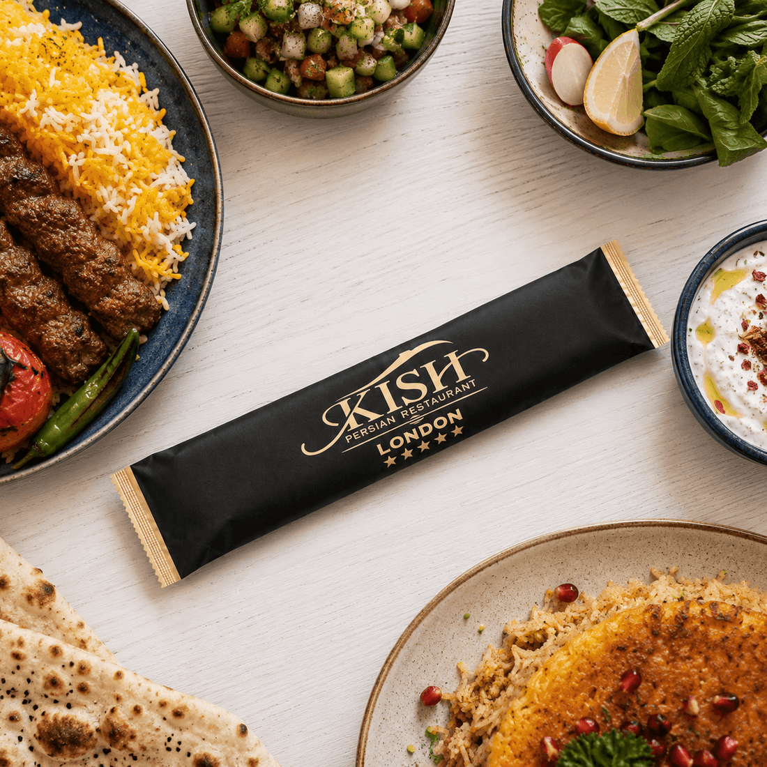 Custom printed Kish Restaurant packaging accessory displayed alongside Persian food, showcasing bespoke branded packaging.