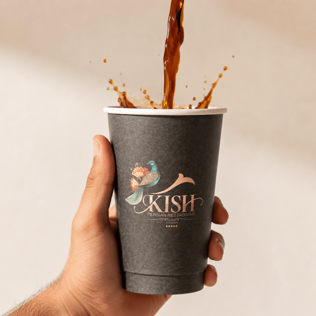 Kish Persian Restaurant branded black takeaway coffee cup being filled with a hot drink.