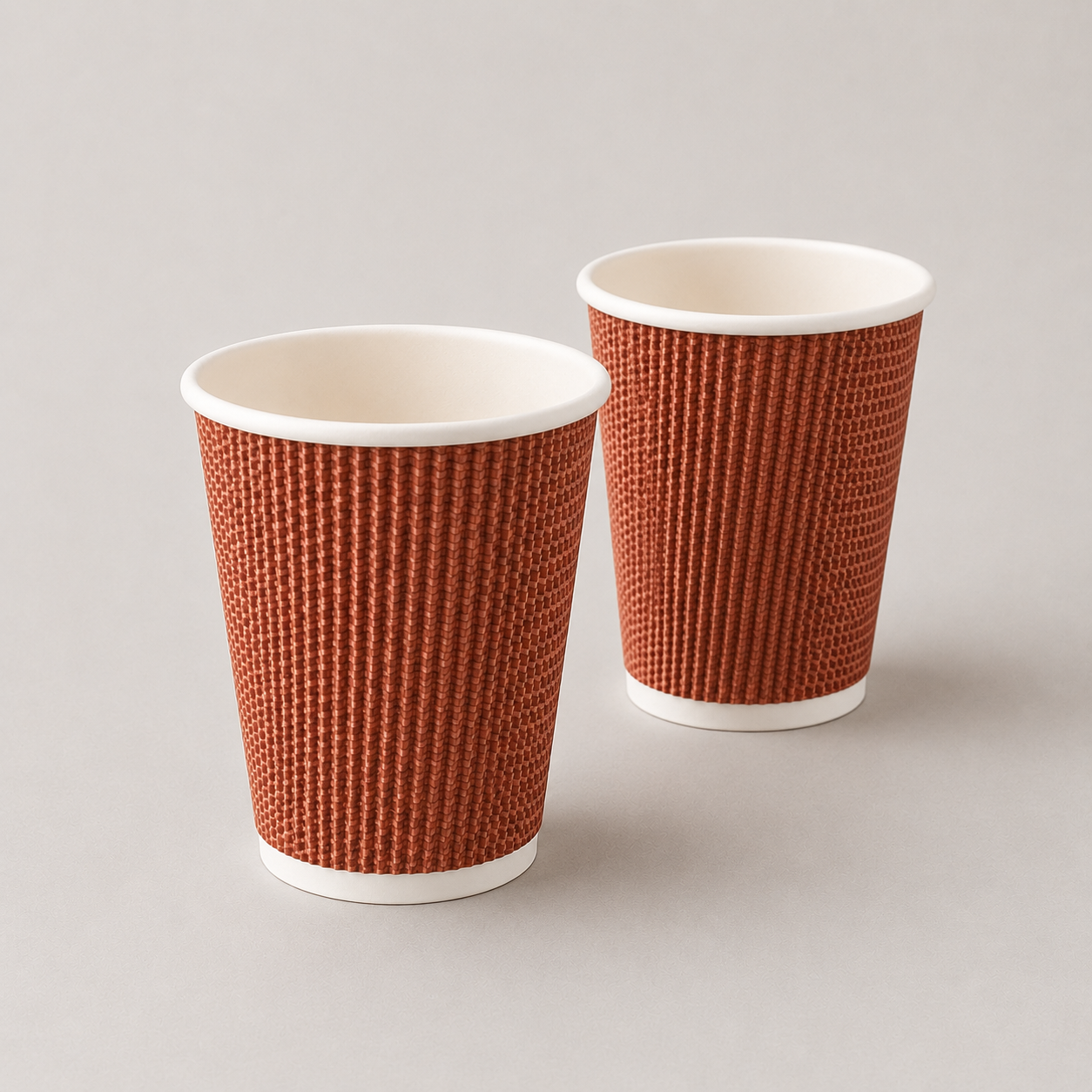 Two textured paper cups with a rust-orange exterior and white interiors, standing on a light gray background.
